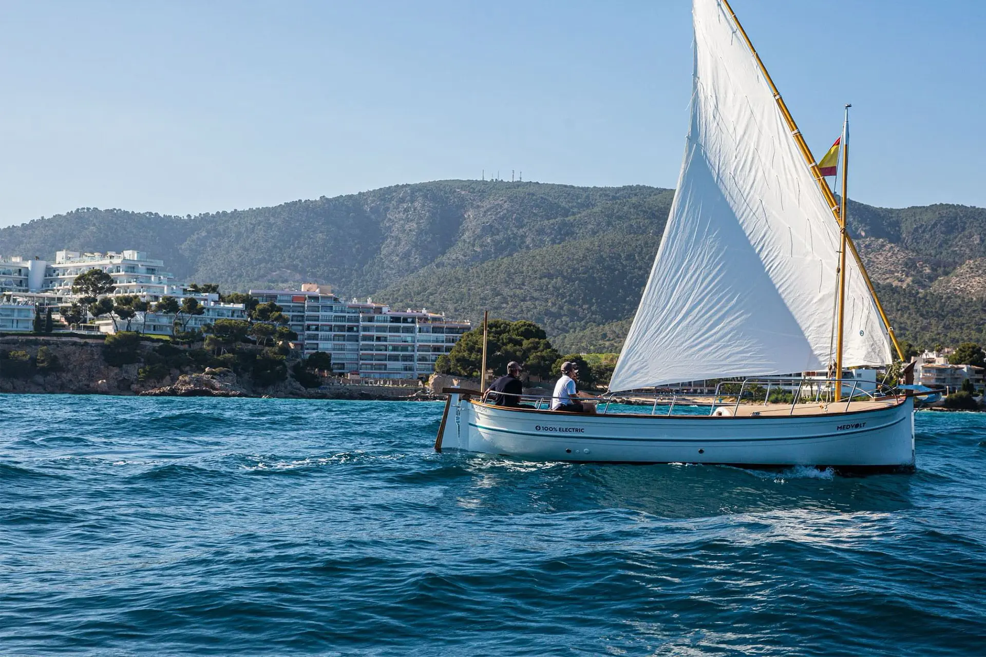 Llaut navegando con vela desplegada frente a la costa mallorquina